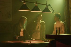 A group of two men and a girl playing pool at a bar